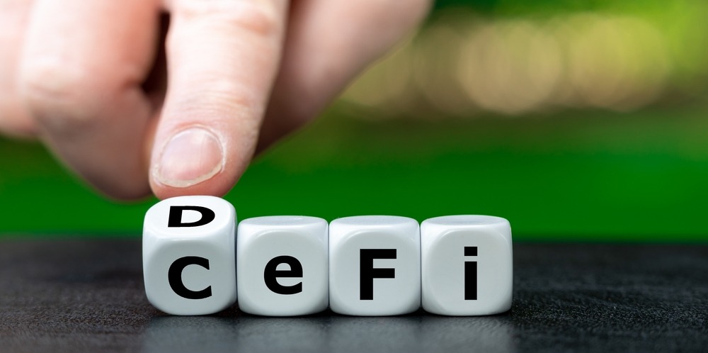 Hand turns dice and changes the expression "CeFi" (centralized finance) to "DeFi" (decentralized finance).