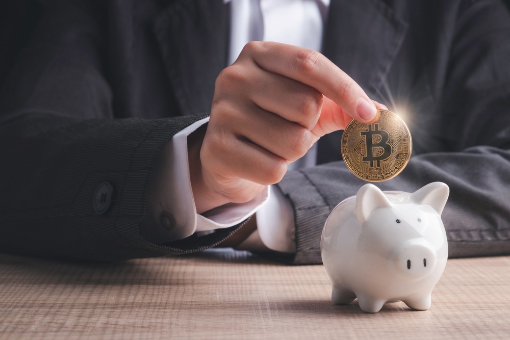 Bitcoin investment concept. Businessman hand holding gold coin cryptocurrency digital money putting into piggy bank on table in black background.